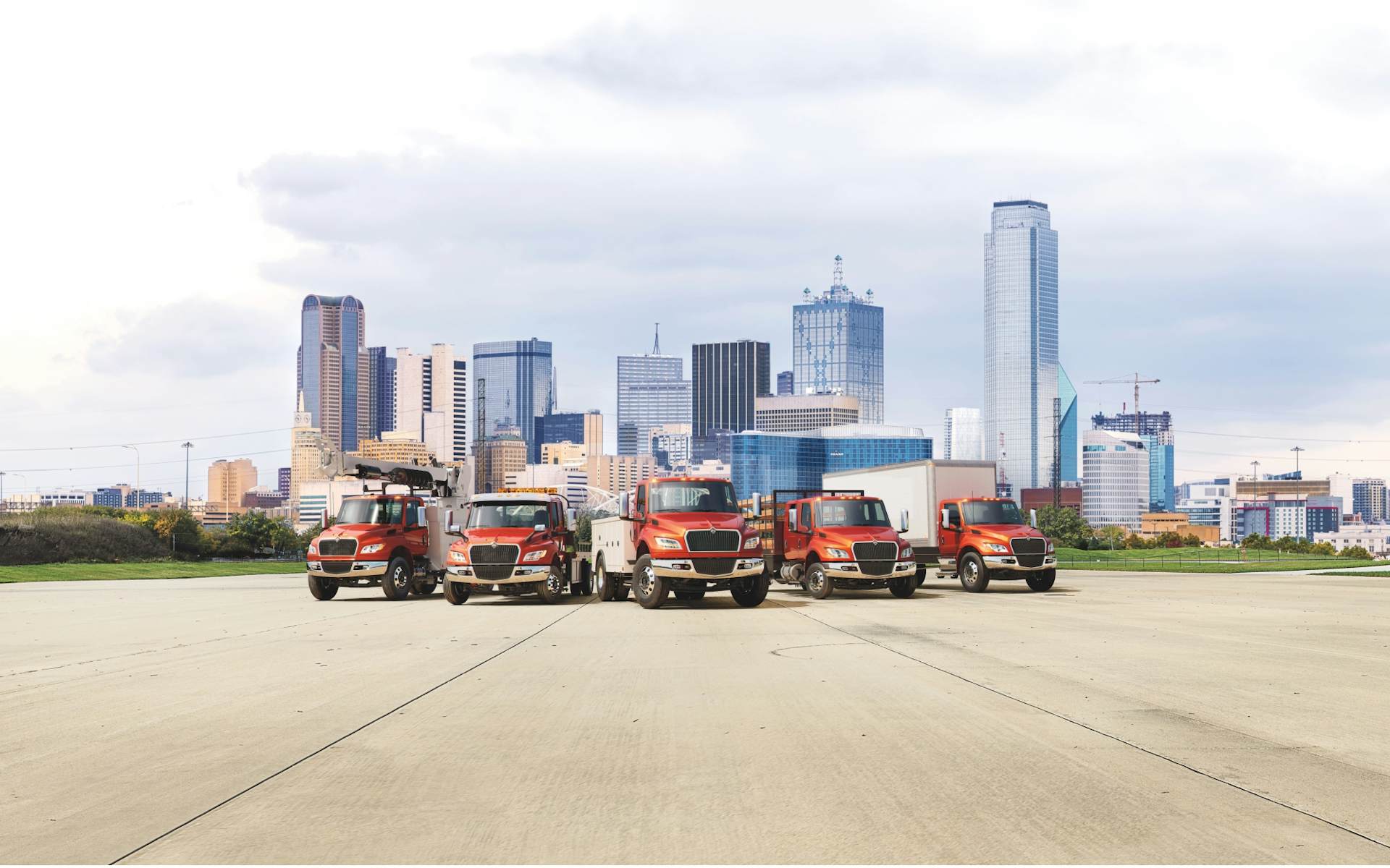 Five red MV Series Commercial Trucks parked in a row in front of a city landscape